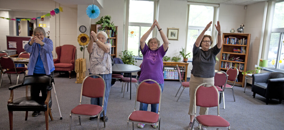 4 older adults exercising by chairs